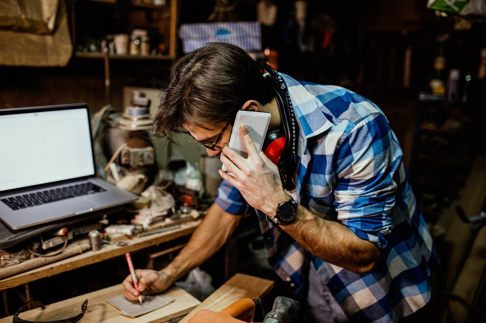 Male carpenter on phone and laptop at the workshop